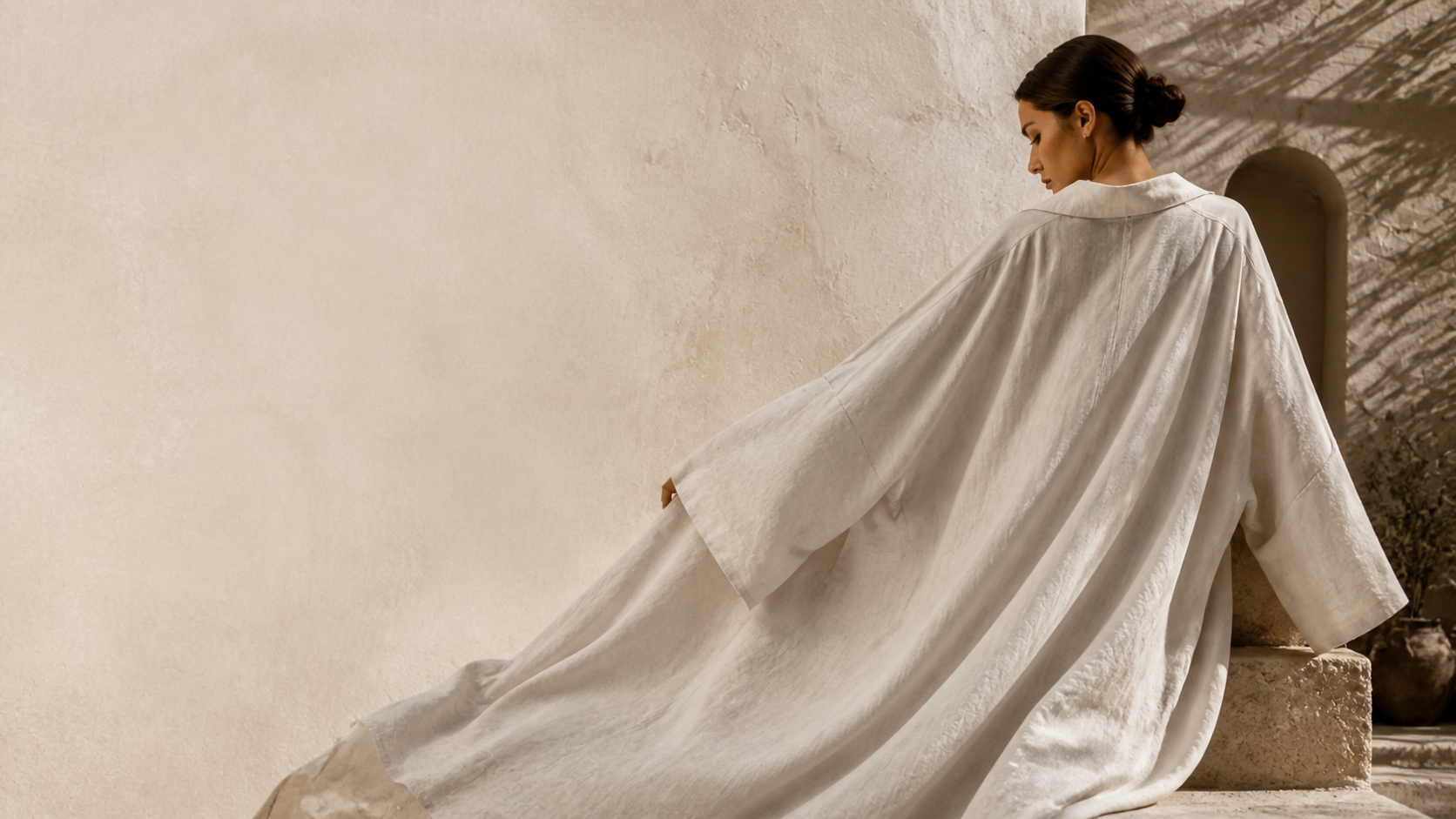 Mujer con tunica amplia de lino natural junto a una pared de textura calida
